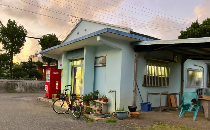 夕暮れの集落の共同売店。店先に自転車と赤い自動販売機