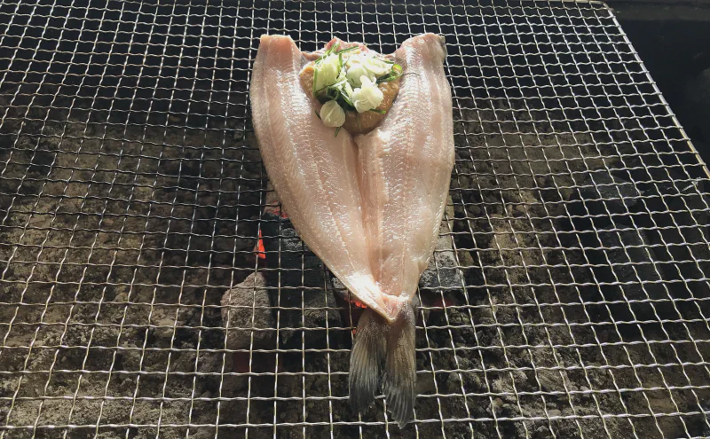 焼き網の上のホッケ。開いた身に味噌と薬味がのっている